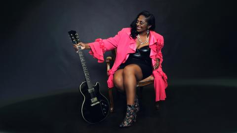 Claudette King sentada y sosteniendo una guitarra mientras sonríe